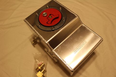 2003 Ford Crown Victoria - polished aluminum fuel cell sits on a sheet, its red Moroso flip-up filler cap open and a bag of brass fittings alongside.