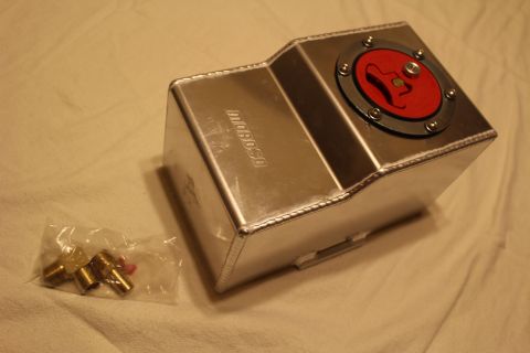 2003 Ford Crown Victoria - welded aluminum fuel cell with a red flip-up filler cap on its angled top, shown next to a bag of brass AN fittings.