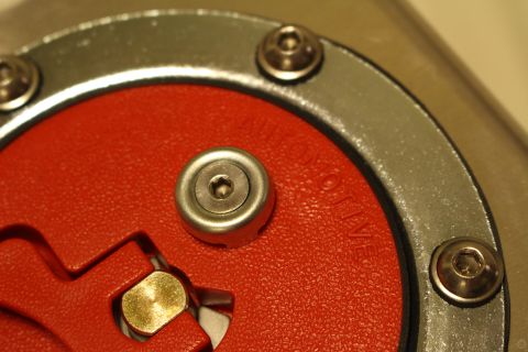 2003 Ford Crown Victoria - Macro shot of a red anodized flip-up fuel cap with a brass center fitting and AUTOMOTIVE text embossed on the rubber surround.