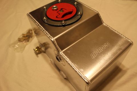 2003 Ford Crown Victoria - polished aluminum fuel cell with a red flip-up cap, Moroso side logo and brass petcock, next to a bag of small parts.