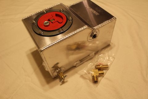 2003 Ford Crown Victoria - welded aluminum fuel cell with red flip-up cap, a side bung and brass petcock, displayed beside bagged brass fittings.