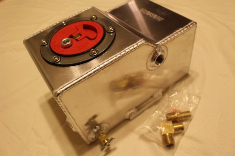 2003 Ford Crown Victoria - polished aluminum fuel cell with red flip-up cap and faint Moroso logo, brass fittings installed and bagged spares nearby.