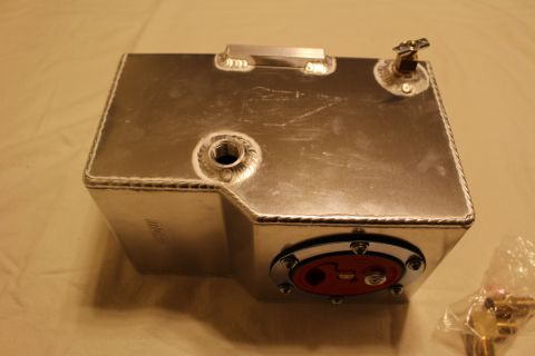 2003 Ford Crown Victoria - aluminum fuel cell shows a recessed carry handle, welded threaded bungs and a brass valve, with the red quick-fill cap visible at the base.