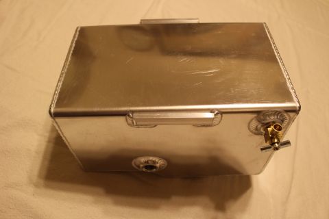 2003 Ford Crown Victoria - brushed aluminum fuel cell rests on a sheet, showing welded threaded bungs, a recessed carry handle, and a brass valve fitting.