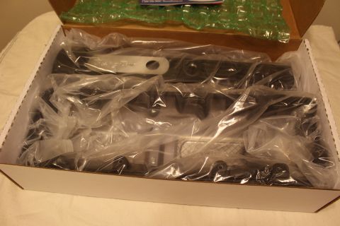 2003 Ford Crown Victoria - close-up inside a shipping box shows dark automotive parts wrapped in plastic, with a white labeled tag among them.