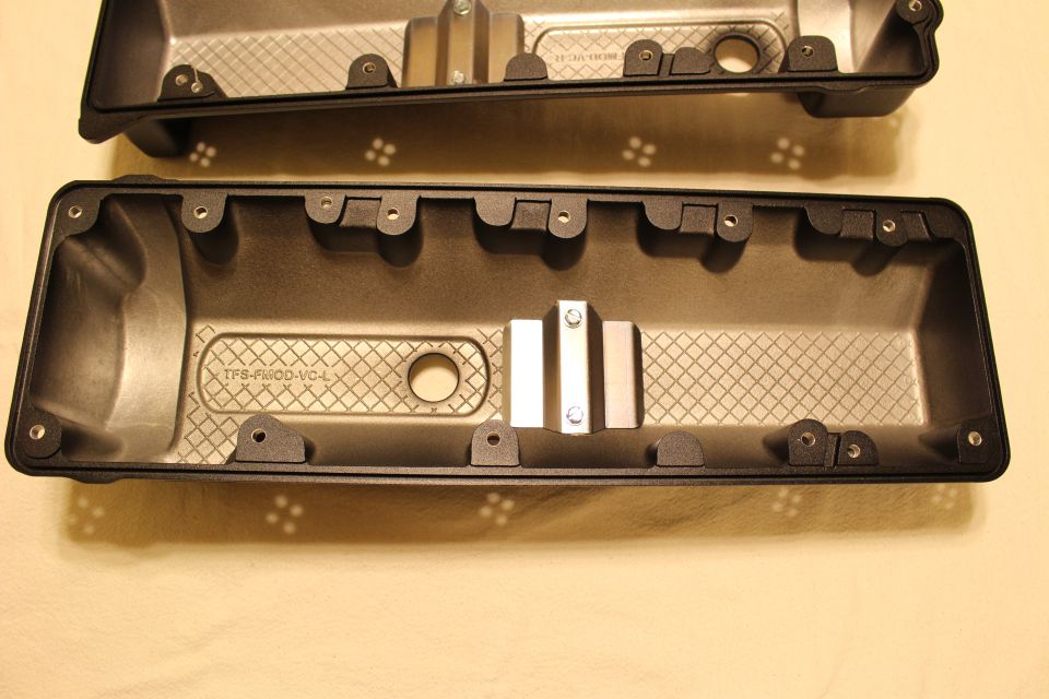 Black plastic valve cover cast 'TFS-FMOD-VC-L' shown interior-up with a metal clip