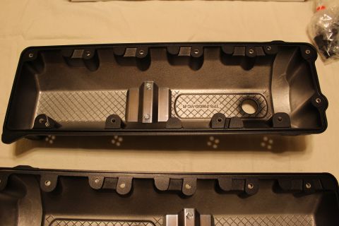 2003 Ford Crown Victoria - black plastic valve cover cast 'TFS-FMOD-VC-R' lies interior-side-up beside its mate, with a bag of hardware at the edge.
