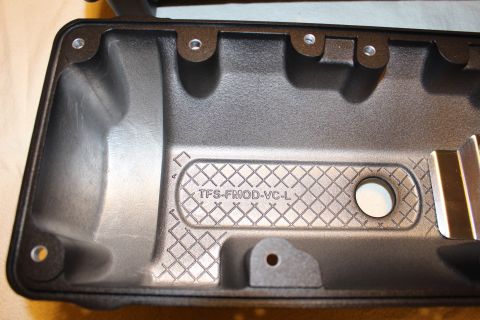 2003 Ford Crown Victoria - close-up of a black plastic valve cover interior shows the cross-hatched casting and embossed text 'TFS-FMOD-VC-L'.