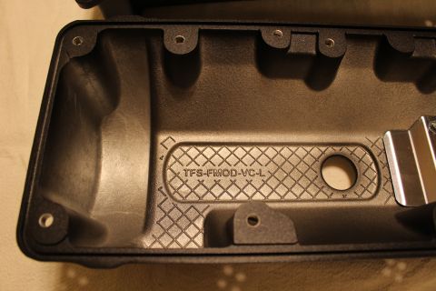 2003 Ford Crown Victoria - close-up of a black plastic valve cover interior shows cross-hatched casting, embossed 'TFS-FMOD-VC-L', and a polished metal clip.