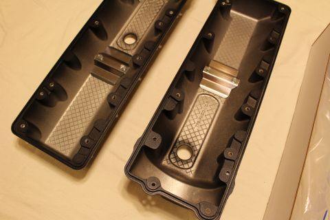 2003 Ford Crown Victoria - Underside view of two black valve covers, one showing a machined metal oil-fill collar and crosshatched internal baffling.
