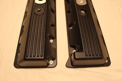 2003 Ford Crown Victoria - Close-up of the lower ends of two black valve covers showing vertical fin ribbing and rounded end caps.