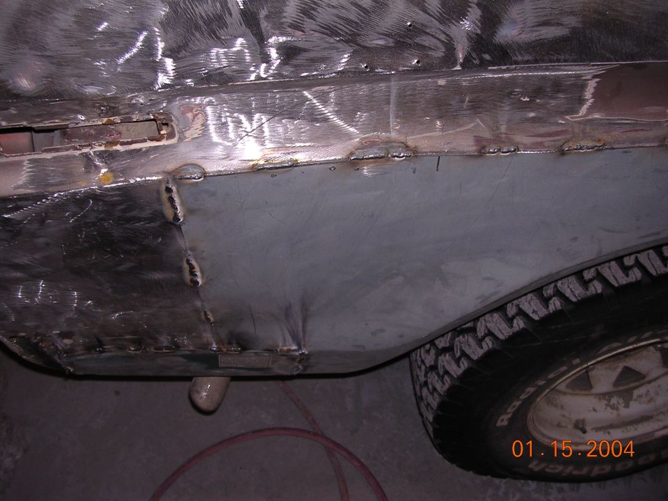 Bare-metal welded body panel and patch repair above a tire on a vehicle in a shop