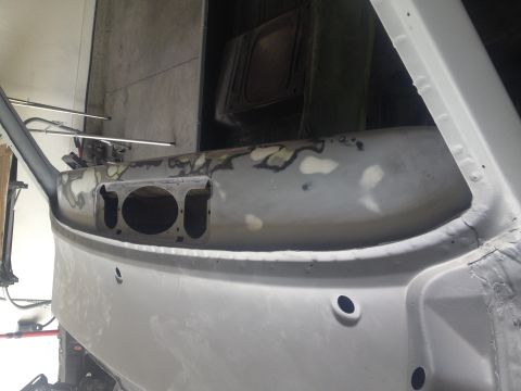 Bare primer-gray vehicle cowl and firewall panel under bodywork in a garage