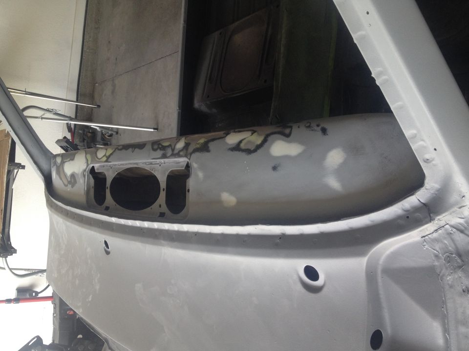 Bare primer-gray vehicle cowl and firewall panel under bodywork in a garage