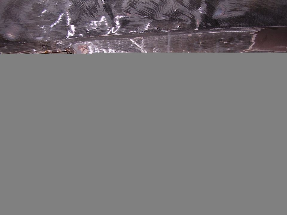 Bare ground-down sheet metal panel with grinding swirls, drilled holes, and rust spots