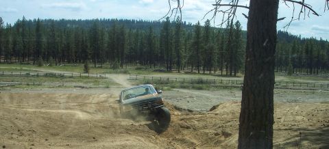 2005 Jeep Wrangler - A truck navigates a challenging off-road course, dust billowing around its tires.