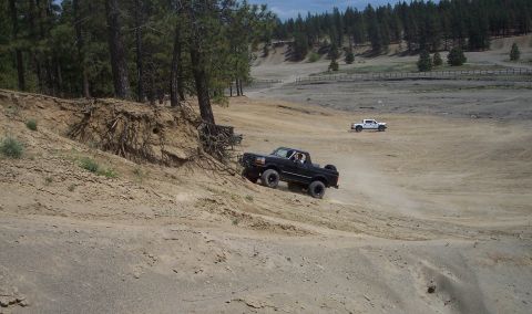 2005 Jeep Wrangler - A black pickup truck navigates a sandy incline in an off-road area, with another vehicle visible in the distance.