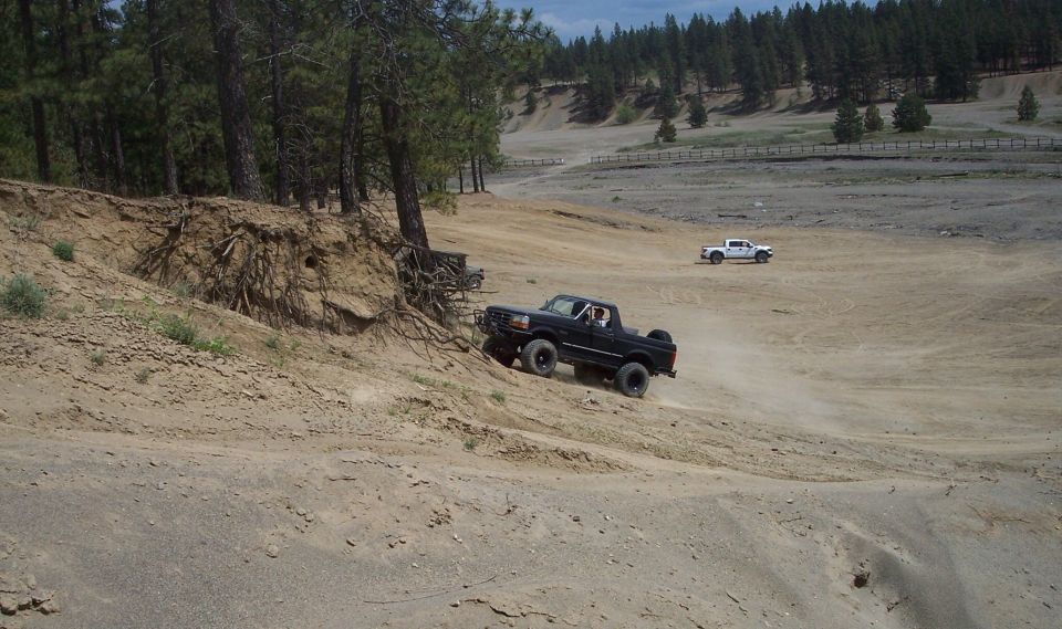 Black pickup truck driving on a dirt hill, with a white pickup truck in the background