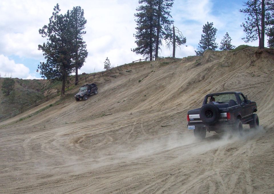 Two off-road vehicles driving up a steep sand dune, one in the foreground kicking up dust
