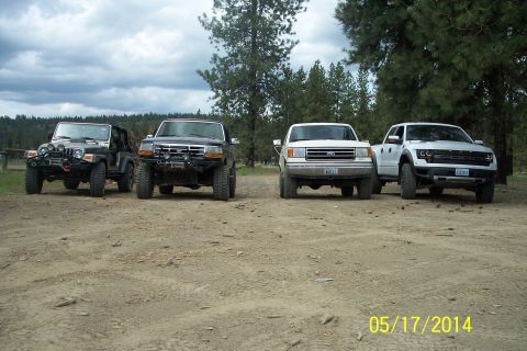 2005 Jeep Wrangler - Four off-road vehicles are lined up on a dirt lot with trees in the background.