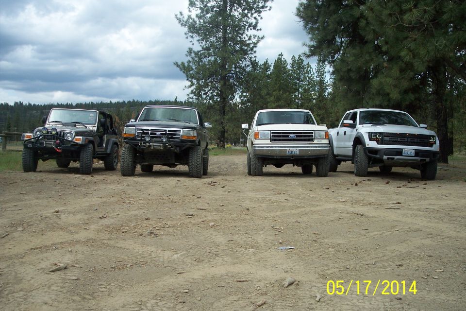 Jeep, black Ford truck, white Ford truck, and white Ford Raptor parked on dirt