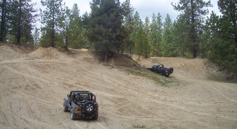 2005 Jeep Wrangler - Two off-road vehicles navigate a sandy terrain with trees in the background.