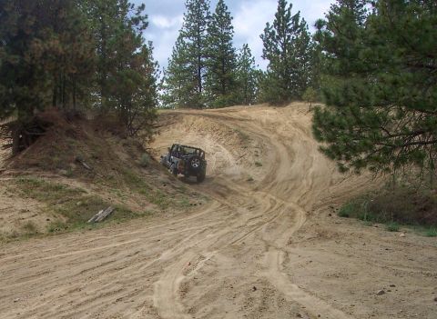 2005 Jeep Wrangler - A black Jeep Wrangler navigates a winding dirt path on a sandy hill, kicking up dust as it climbs.