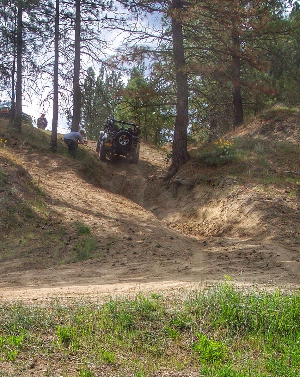Jeep Wrangler driving up a dirt hill with trees around