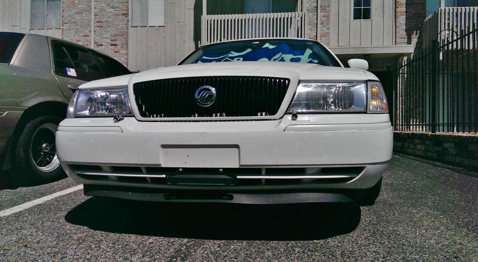 White Mercury Grand Marquis parked next to a tan sedan, front view