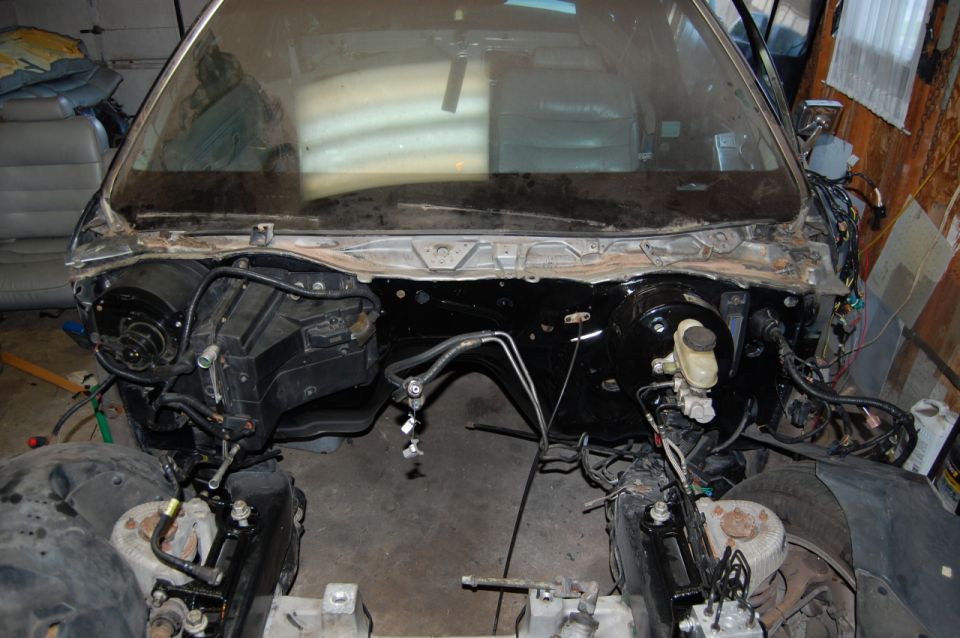 Front clip of a vehicle stripped down in a garage exposing firewall, brake booster and wiring