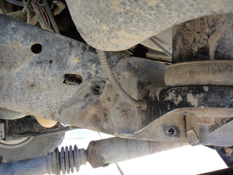 Close-up of dirty truck frame with suspension parts visible, including a shock absorber and drive shaft boot
