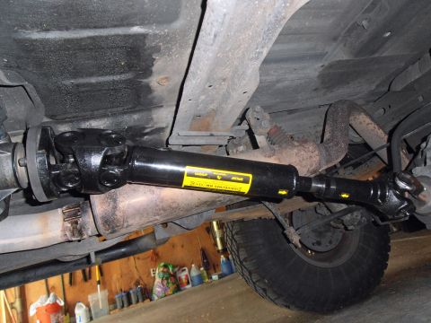 1990 Ford Bronco - Underbody shot of a newly installed black driveshaft with heavy-duty double-cardan and single U-joints, wearing a yellow driveline balance/…