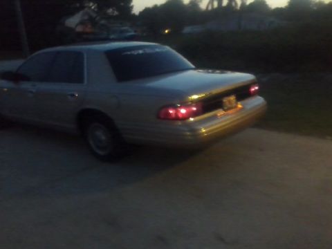 1997 Mercury Grand Marquis - The rear of a silver sedan is visible from a low angle at dusk, with its taillights on.