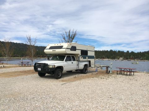 1997 Dodge 3500 - A white 1997 Dodge 3500 pickup truck equipped with a camper shell is parked at a campsite next to a lake.