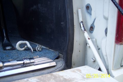 1990 Ford Bronco - Close-up of a tailgate torsion bar and associated hardware, with a socket wrench visible on the carpeted floor.