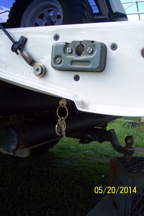 1990 Ford Bronco - The rear of a vehicle shows a tailgate latch, keys, and a trailer hitch assembly.