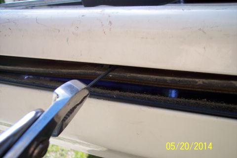 1990 Ford Bronco - A close-up view shows a metal rod being manipulated into a tailgate torsion bar mechanism.