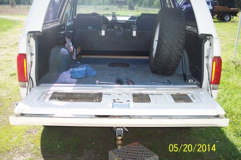 1990 Ford Bronco - The open tailgate reveals the interior of a white 1990 Ford Bronco, with a spare tire and tools inside.