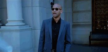 2000 Mercury Grand Marquis - A man wearing a suit and sunglasses walks past a building with large columns.
