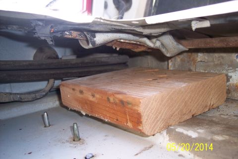 1990 Ford Bronco - Close-up of a tailgate torsion bar mechanism, supported by a wooden block. The Supermotors.net logo is visible in the lower right corner.