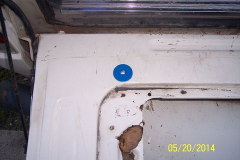 1990 Ford Bronco - Close-up of a white tailgate section showing rust and a blue washer, with a website logo in the corner.