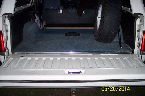 1990 Ford Bronco - The rear cargo area of a vehicle is shown with the tailgate down, revealing a spare tire and carpeted floor.