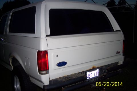 1990 Ford Bronco - The rear of a white 1990 Ford Bronco is visible, with a hardtop and a license plate reading 486-YJD.