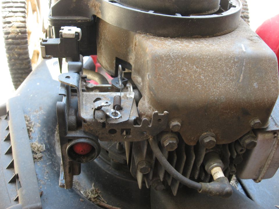 Close-up of a lawn mower engine with a red primer bulb and spark plug