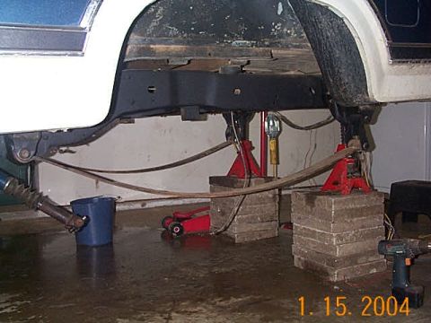 1986 Ford Bronco - Vehicle frame and suspension components are supported by jack stands and blocks.