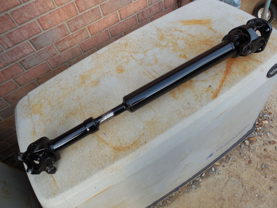 Black driveshaft with U-joints resting on a rust-stained white cooler