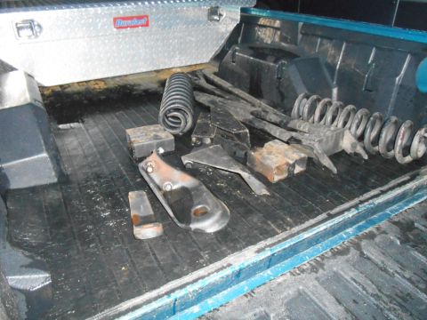 1994 Ford Bronco - Various lift kit components, such as springs and brackets, are stored in the bed of a pickup truck alongside a toolbox.