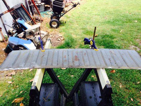 1979 Ford Bronco - A tailgate is clamped to sawhorses in a yard, with various parts and equipment in the background.