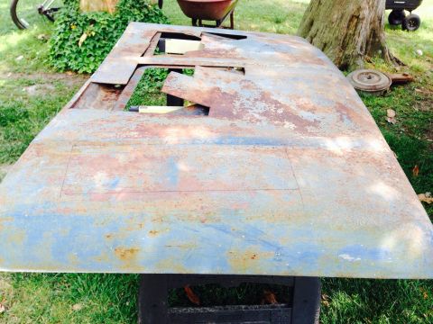 1979 Ford Bronco - A heavily rusted car hood with cutouts rests outdoors on sawhorses.