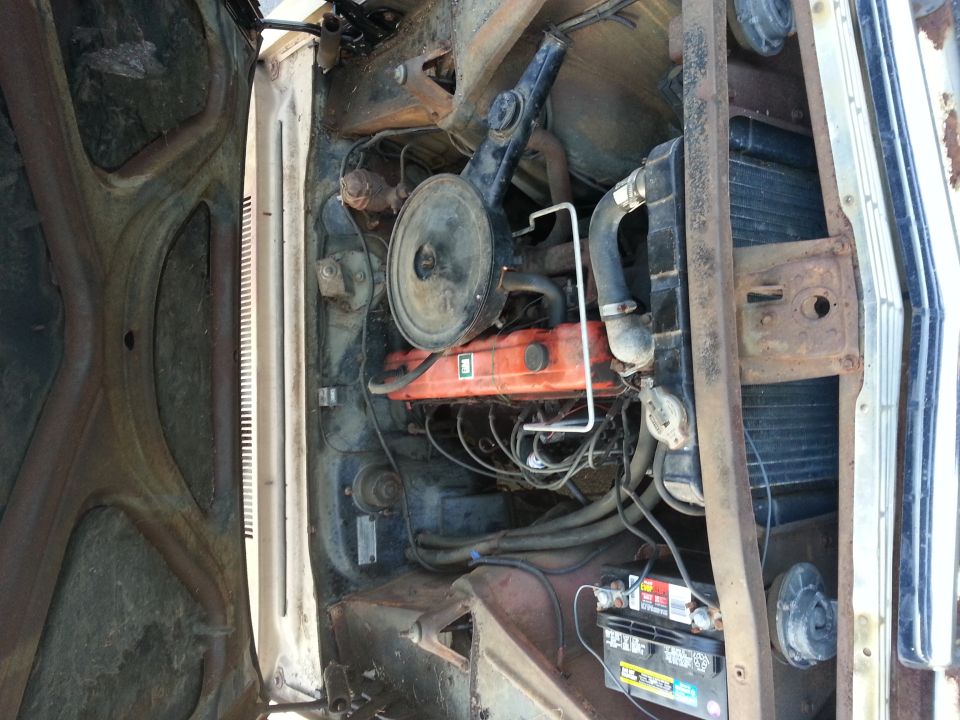 Car's engine bay with V8 engine, air cleaner, radiator, and battery visible